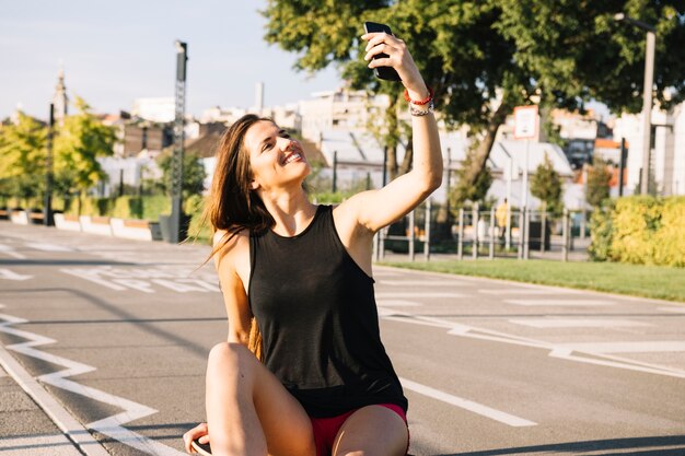 Szczęśliwy kobiety obsiadanie na deskorolka bierze selfie z telefonem komórkowym