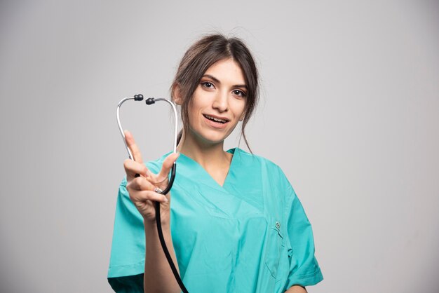 Szczęśliwy lekarz pokazując stetoskop na szaro