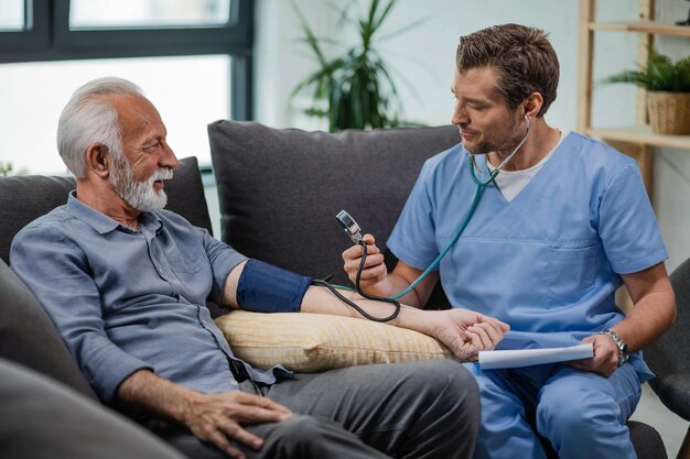 Szczęśliwy lekarz rodzinny mierzący ciśnienie krwi dojrzałego mężczyzny podczas wizyty domowej
