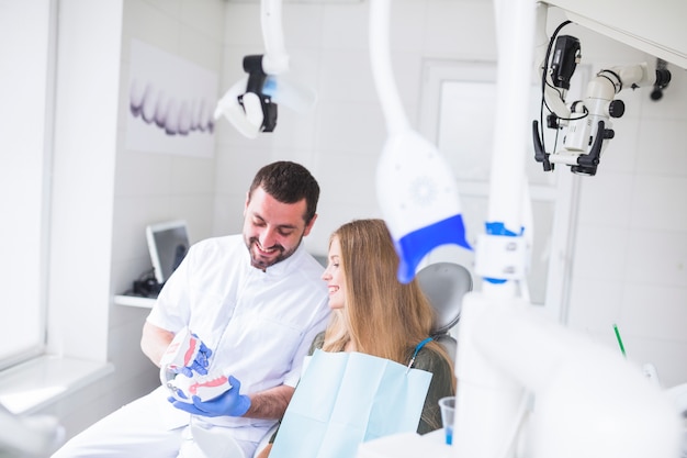 Szczęśliwy męski dentysta pokazuje zębu modela pacjent