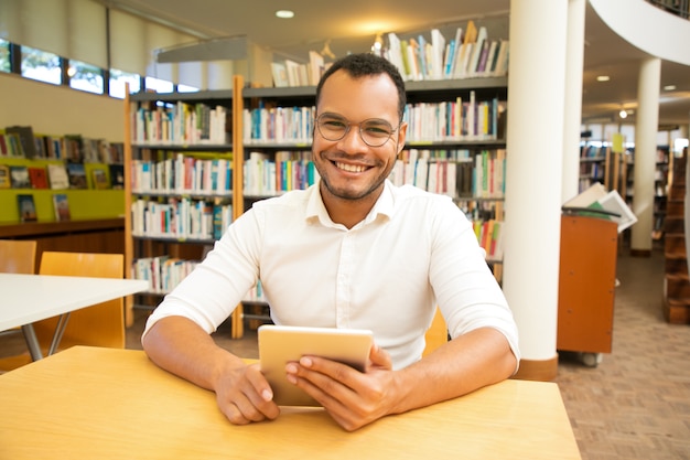 Szczęśliwy męski klient używa publicznego hotspot Wi-Fi w bibliotece