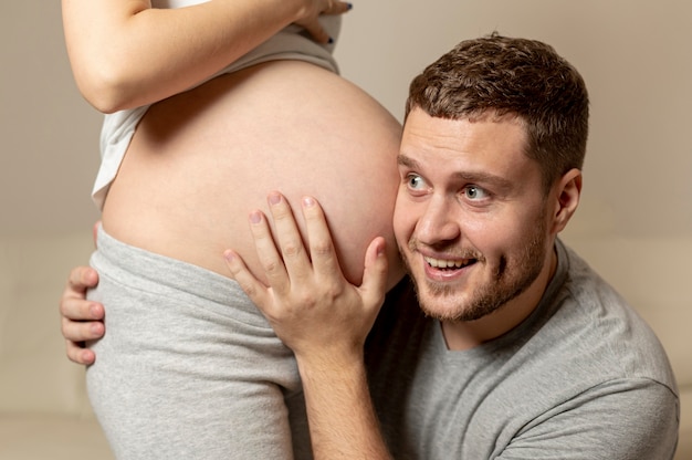 Bezpłatne zdjęcie szczęśliwy mężczyzna słucha brzucha ciężarnej żony