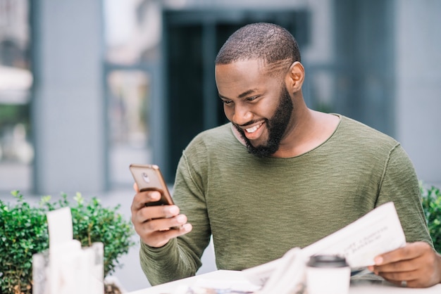 Szczęśliwy mężczyzna używa smartphone w kawiarni