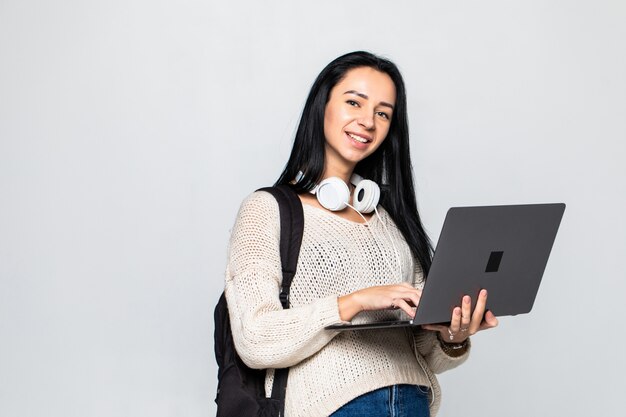 Szczęśliwy młodej kobiety mienia laptop nad popielatą ścianą i