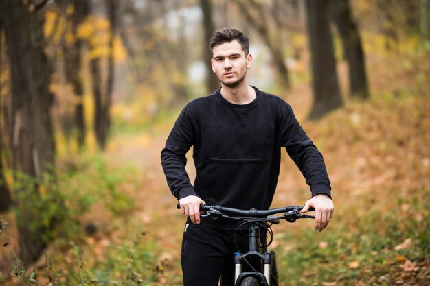 Szczęśliwy młody cyklisty mężczyzna jedzie na jego bicyklu na szkoleniu w jesień lesie
