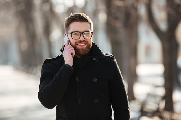 Szczęśliwy młody człowiek opowiada na telefonie komórkowym outdoors w zimie