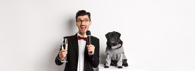Bezpłatne zdjęcie szczęśliwy młody człowiek wygłasza przemówienie i podnosi szklaną szampańską pozycję z uroczym czarnym psem w partyjnej współpracy