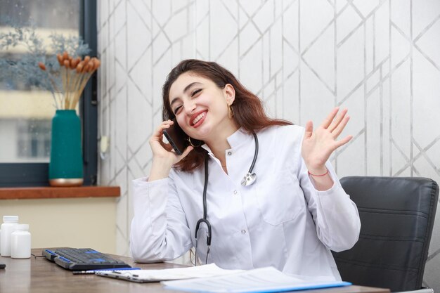 Szczęśliwy młody lekarz siedzi w biurze i rozmawia przez telefon Zdjęcie wysokiej jakości