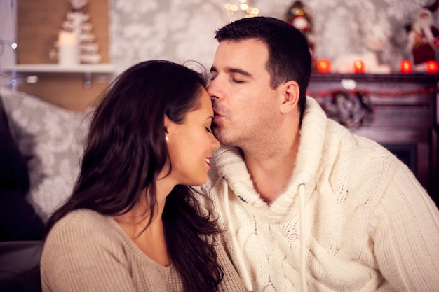 Szczęśliwy młody mąż całuje żonę w czoło w Boże Narodzenie. Świąteczna dekoracja.