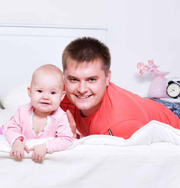 Szczęśliwy młody ojciec z uśmiechniętym dzieckiem leżącym na łóżku w sypialni