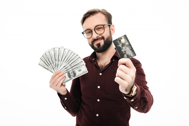 Szczęśliwy myślący młody człowiek trzyma pieniądze i kredytową kartę.
