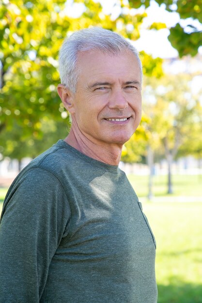 Szczęśliwy pozytywny dojrzały mężczyzna ubrany w sportową koszulkę z długim rękawem, stojący na zewnątrz i uśmiechnięty. Sredni strzał. Dojrzała sportowa osoba lub koncepcja aktywnego stylu życia
