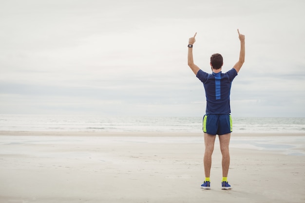 Szczęśliwy sportowiec stojący na plaży z podniesionymi rękami