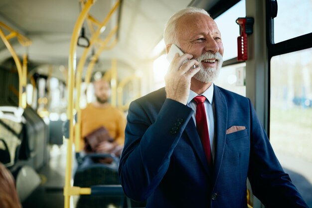 Szczęśliwy starszy biznesmen rozmawia przez telefon podczas dojazdu do pracy autobusem