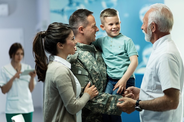 Bezpłatne zdjęcie szczęśliwy starszy lekarz rozmawia z małym chłopcem, który przyszedł z matką i ojcem wojskowym do kliniki. skupiamy się na wojskowym