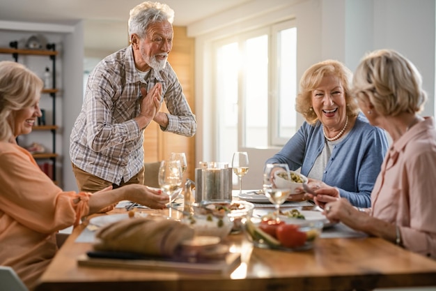 Szczęśliwy starszy mężczyzna cieszący się podczas rozmowy ze swoimi koleżankami podczas obiadu w domu
