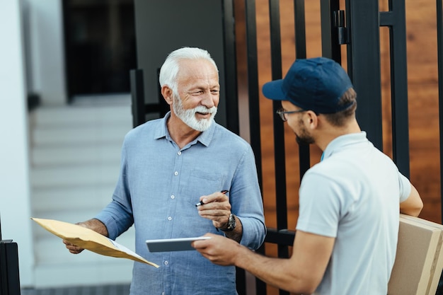 Szczęśliwy starszy mężczyzna komunikujący się z dostawcą podczas podpisywania na cyfrowym tablecie w celu dostawy do domu