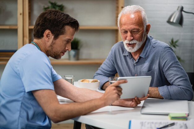 Szczęśliwy starszy pacjent i jego lekarz patrzący na wyniki badań medycznych na touchpadzie podczas wizyty lekarskiej