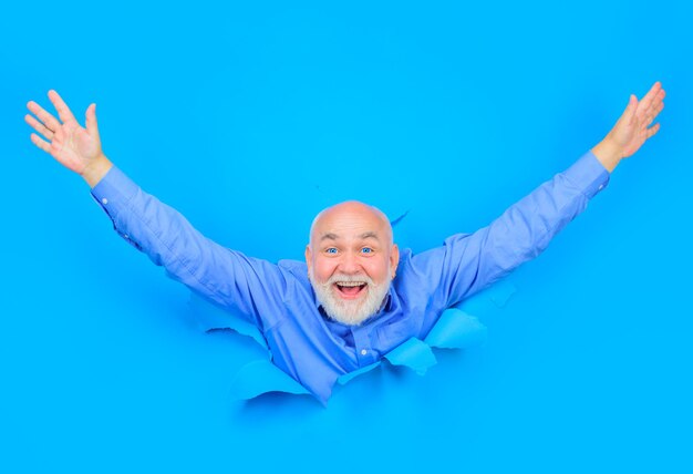 Szczęśliwy stary brodaty mężczyzna przez dziurę w niebieskim papierze miejsce na reklamę sezon wyprzedaży zniżki
