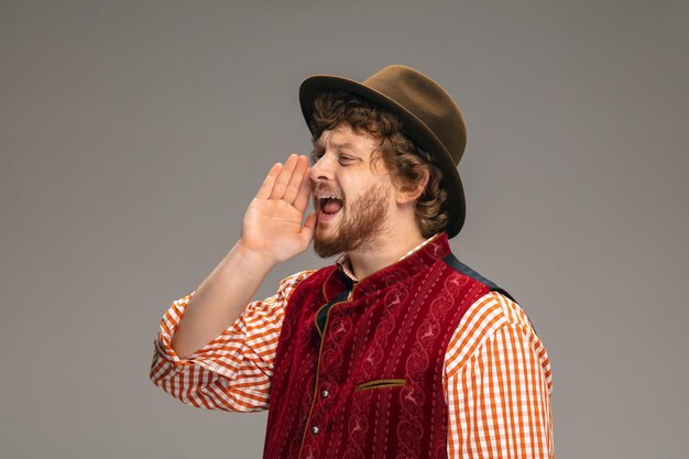 Szczęśliwy uśmiechnięty mężczyzna ubrany w tradycyjny austriacki lub bawarski strój, gestykuluje na szarym tle