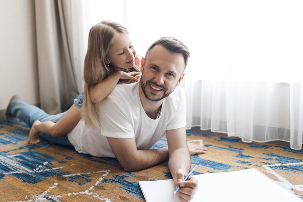 szczęśliwy uśmiechnięty ojciec i jego córka rysują i odrabiają prace domowe w domu
