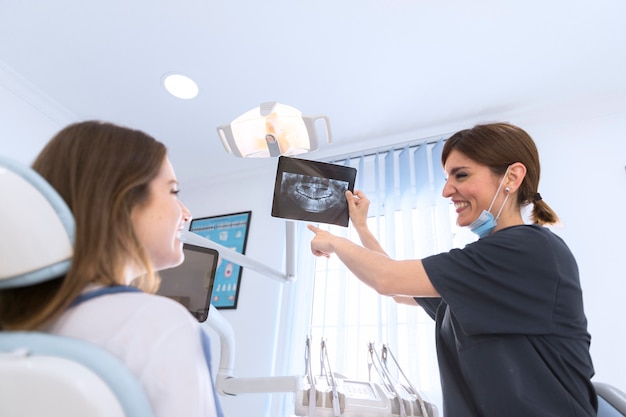 Szczęśliwy uśmiechnięty żeński dentysta pokazuje stomatologicznego promieniowanie rentgenowskie pacjent