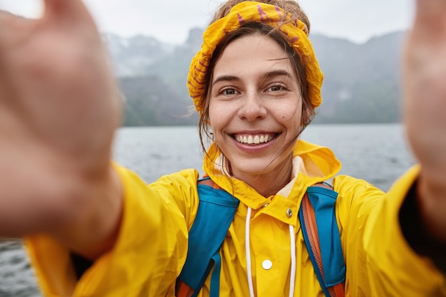 Bezpłatne zdjęcie szczęśliwy wędrowiec lubi wyprawy pełne przygód, robi selfie na tle majestatycznego górskiego krajobrazu