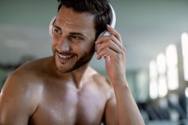 Szczęśliwy wysportowany mężczyzna cieszący się muzyką na słuchawkach na siłowni