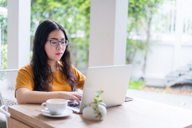 Szczęśliwy z azjatyckich niezależnych ludzi biznesowych kobieta dorywczo pracująca z laptopem z filiżanką kawy i smartfonem w kawiarni jak tło, koncepcja komunikacji