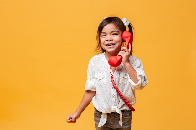 Szczęśliwy z podnieceniem małej dziewczynki dziecko opowiada czerwonym retro telefonem.