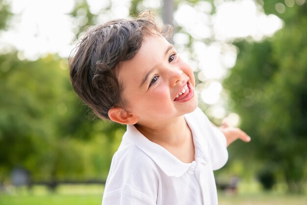 Szczęśliwy zabawny uroczy chłopiec tańczy, śmieje się, bawi się w letnim parku, uśmiecha się i odwraca wzrok. Strzał zbliżenie. Koncepcja dzieciństwa