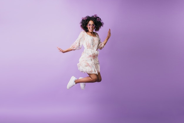 Szczupła afrykańska kobieta w białych trampkach skacze i śmiejąc się. Wewnątrz zdjęcie wesołej czarnej dziewczyny tańczącej.