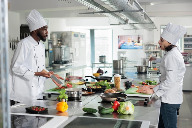 Szef i zastępca szefa kuchni rozmawiają o tym, jaki przepis przygotować na kolację w eleganckiej restauracji. Wykwalifikowani eksperci gastronomii gotują dania dla smakoszy w profesjonalnej kuchni.