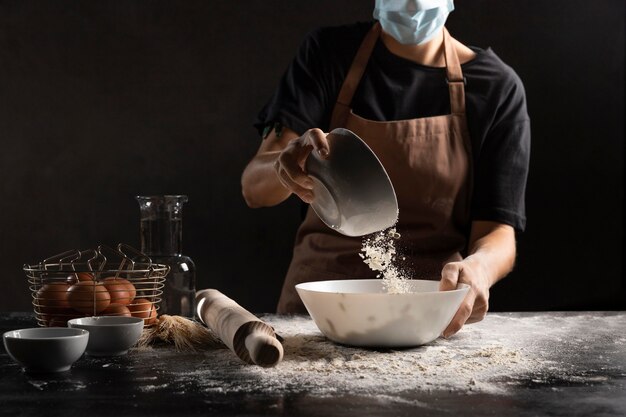 Szef kuchni dodaje mąkę do miski w celu wytworzenia ciasta