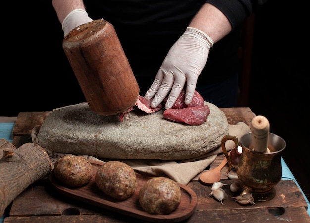 Szef kuchni mielenia surowego mięsa z drewnianym młotem na kamieniu