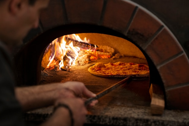 Bezpłatne zdjęcie szef kuchni pod dużym kątem piecze pizzę w piecu opalanym drewnem