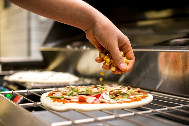 Szef kuchni stawia kukurydzę na cieście do pizzy pokrytym sosem pomidorowym