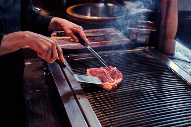 Szef kuchni w mundurze gotuje pyszny stek wołowy w kuchni w restauracji