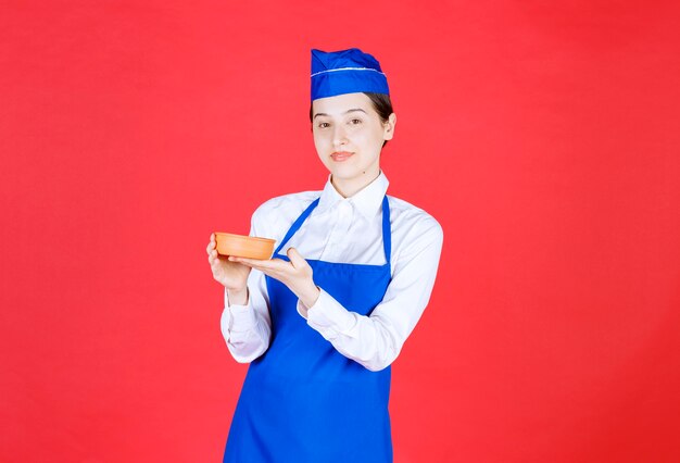 Szef kuchni w niebieskim fartuchu trzyma miskę ceramiki.