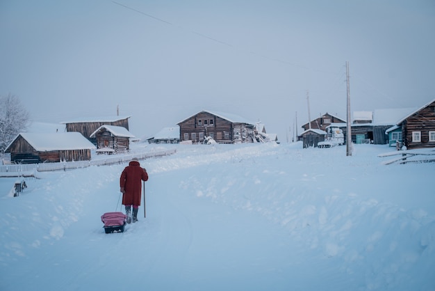 Szerokie ujęcie przedstawiające wioskę i osobę w czerwonym płaszczu idącą przez gęsty śnieg w zimny dzień