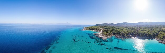 Szerokie ujęcie wybrzeża Morza Egejskiego z niebieską, przezroczystą wodą, zielenią wokół, widok pamoramy z drona, Grecja
