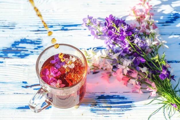 Szklana filiżanka herbaty z polnymi kwiatami i bukietem na drewnianym stole zbliżenie