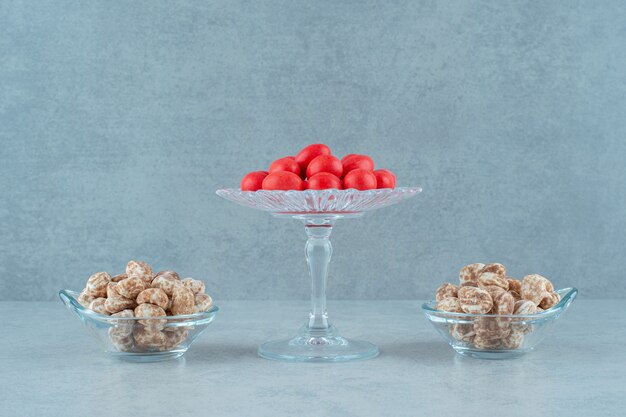 Bezpłatne zdjęcie szklane talerze pełne pysznych pierników i czerwonych słodkich cukierków na białej powierzchni