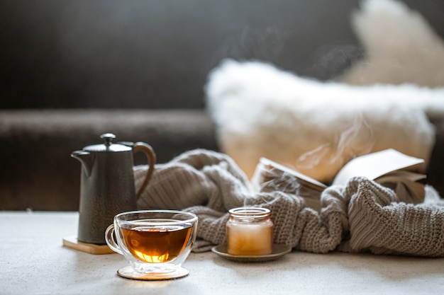 Szklanka herbaty, imbryk, świeczka z dzianiną. Pojęcie domowego komfortu i ciepła.