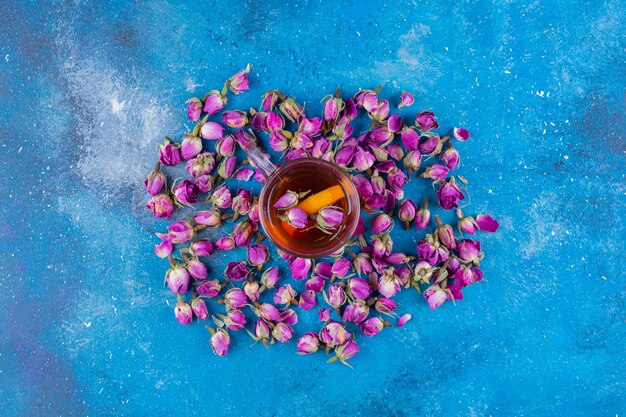 Bezpłatne zdjęcie szklanka herbaty z kwitnącymi różami umieszczona na niebieskim stole.