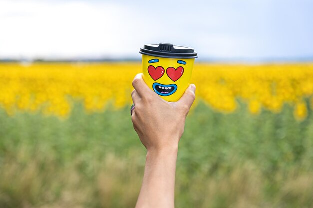 Bezpłatne zdjęcie szklanka kawy w kobiecej dłoni na tle słoneczników