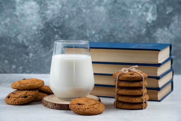 Szklanka mleka, słodkie ciasteczka i książka na marmurowym stole.