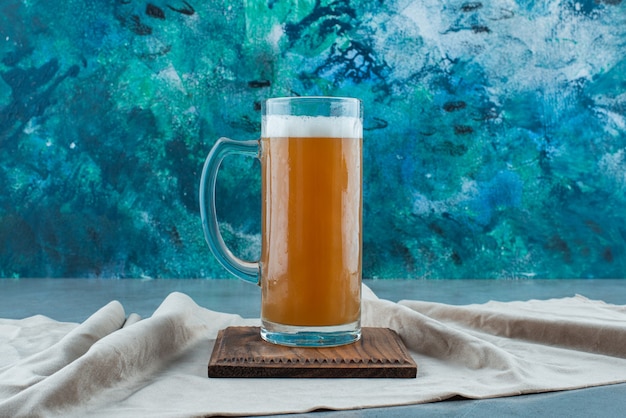 Szklanka piwa na desce na ręczniku, na niebieskim stole.