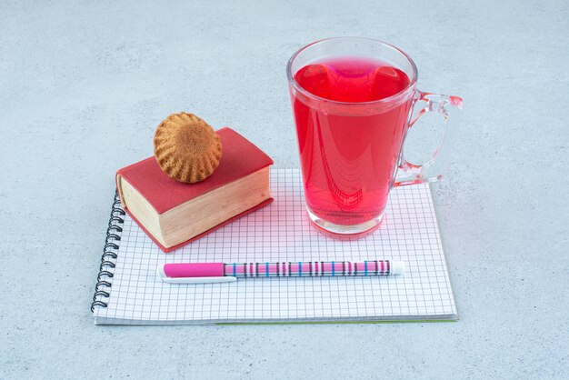 Bezpłatne zdjęcie szklanka soku, ciasto, zeszyt i długopis o niebieskiej powierzchni.