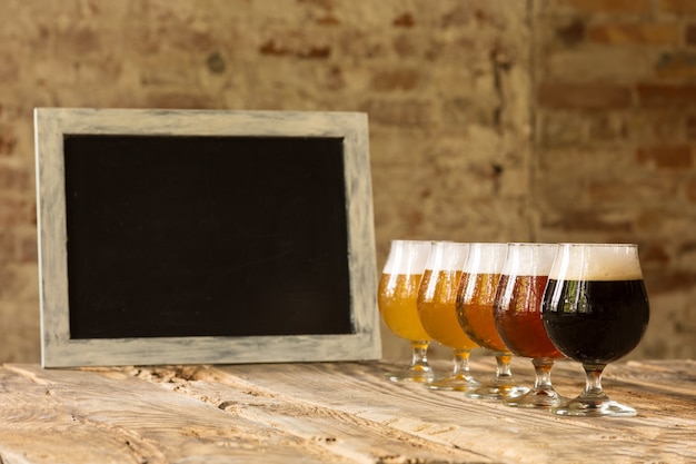 Bezpłatne zdjęcie szklanki różnych rodzajów ciemnego i jasnego piwa na drewnianym stole w linii i tablicy